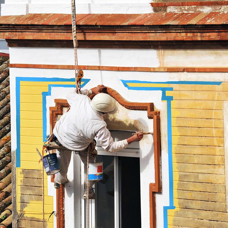 Professional painter and decorator hanging from building while painting on the 14 day blue tape